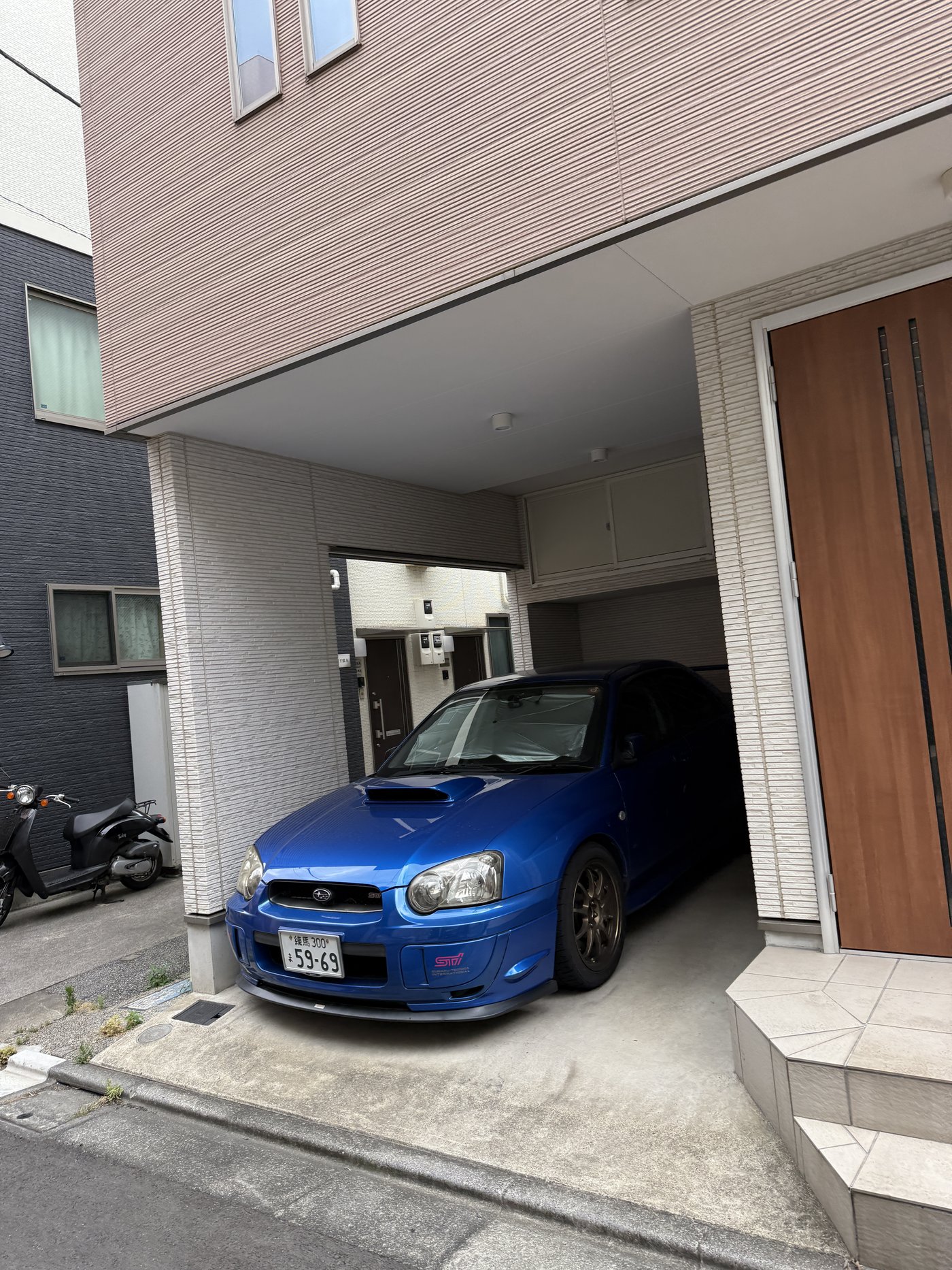 Modré Subaru Impreza WRX STI zaparkované v úzkém vjezdu do domu